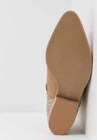 Chaussure à talons hauts en suède marron avec une semelle texturée et un accent scintillant. Le talon est effilé avec une base lisse beige en bas.