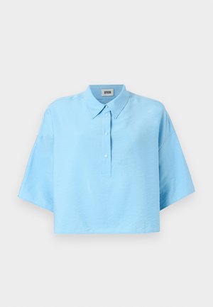 Vaaleansininen lyhythihainen cropattu paita, jossa on kauluskäänne, etupainonappikiinnitys ja lyhyet hihat. Valmistettu sileästä, kevyestä kankaasta.