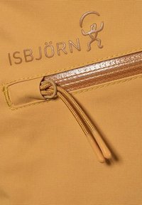 Keltainen kangaskassi, jossa on sileä vetoketjuyksityiskohta. Laidassa on ruskeaksi kohokuvioitu logo ja vaaleammasta sävystä valmistettu vetoketjun vedin.