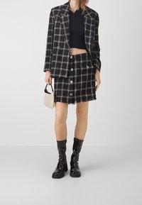 Blazer en tweed avec motif à carreaux noir et rose, associé à une mini-jupe assortie ornée de boutons. Bottes noires brillantes montantes jusqu'aux genoux.