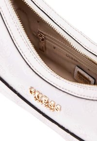 Borsa a tracolla bianca con motivo e hardware dorato, tasca interna con zip e logo "GUESS". Texture liscia e design strutturato.