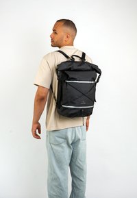 Čierny batoh s rolovacím vrchom, reflexnými detailmi, nastaviteľnými popruhmi a odolným vodoodolným materiálom. Obsahuje predné zipsové vrecko a sťahovaciu šnúrku.