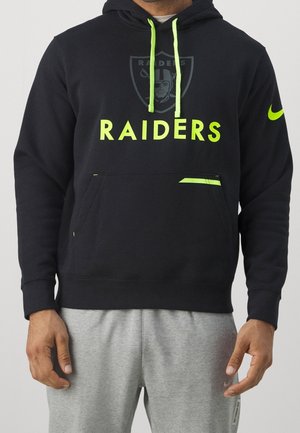 Mann trägt schwarzen Raiders-Hoodie mit neon-grünen Kordeln und Logo, kombiniert mit hellgrauen Jogginghosen.