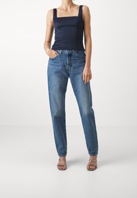 Navy satin top with a square neckline paired with high-waisted light blue jeans. The model wears silver strappy sandals. Plain background.
