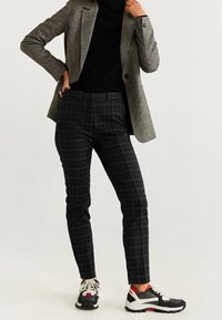 Blazer à carreaux gris porté sur un haut noir, accompagné d'un pantalon noir slim et de baskets noires avec des accents blancs et rouges.
