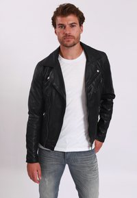 Svart läderjacka med en figursydd design, asymmetrisk dragkedja och breda slag. Kombinerad med en vit t-shirt och ljusblå jeans.