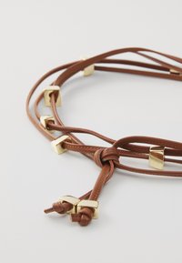 Brown leather cord with gold square accents, intertwined design, smooth texture, and knotted ends. Suitable for a versatile accessory.