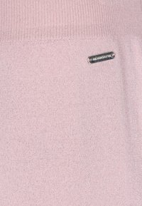 Lichtroze gebreide trui met een zachte textuur, met een glanzende afwerking en een klein metallic label dat op de stof is genaaid.