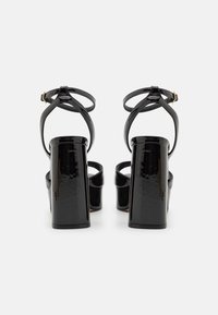 Sandales à plateforme en cuir verni noir avec un talon épais, dotées de brides croisées à la cheville et d'un design élégant. Texture lisse, accents minimalistes.