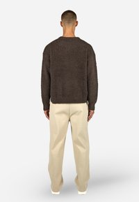 Brązowy, puszysty sweter o luźnym kroju, okrągłym dekolcie i długich rękawach, zestawiony z jasnymi beżowymi spodniami. Prosty krój i widoczne tekstury.