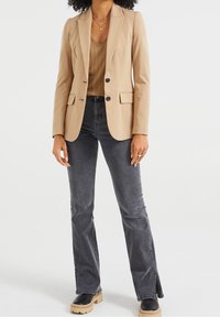 Blazer marrón con dos botones, solapas muesca y bolsillos de solapa, combinado con jeans acampanados gris oscuro y zapatos de plataforma negros.