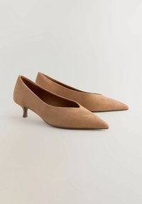 Beige mokasíny na vysokém podpatku s špičatou špičkou a malým blokovým podpatkem. Hladký povrch a minimalistický design.