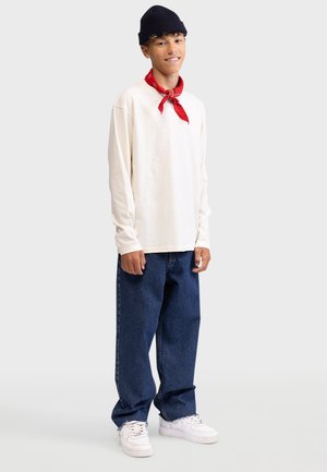 Long-sleeve cream shirt, blue baggy jeans, red bandana, white sneakers, and black knit hat. Casual outfit with simple color palette.