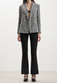 Blazer doppiopetto in tweed nero e bianco, con grandi bottoni argentati e tasche a patta; abbinato a pantaloni neri aderenti e tacchi.