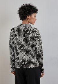 Suéter de patrón en blanco y negro con diseños geométricos, mangas largas y un cuello redondo, hecho de una suave tela texturizada.