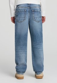 Jeans in denim azzurro chiaro con una vestibilità comoda, dotati di due tasche posteriori e orli risvoltati, che mostrano una texture sbiadita e una linea dritta.