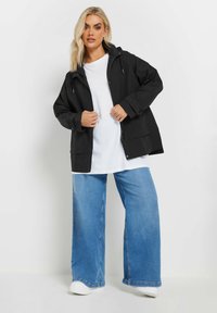 Svart lättviktsjacka med huva, dragkedja framtill och två fickor fram, kombinerat med en vit t-shirt och vida denimjeans.