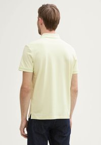 Polo shirt jaune clair en coton doux, doté de manches courtes et d'un col à trois boutons. L'ourlet présente des fentes latérales pour un ajustement décontracté.