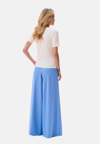 Geribbelde witte top met korte mouwen in combinatie met lichtblauwe wijde broek, met een gladde textuur en losse pasvorm.