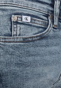 Džínové kalhoty Calvin Klein v modré barvě, zobrazující detailní pohled na kapsu s logem, viditelným šitím a hladkou texturou.