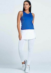 Top athletic blu con gonna a strati bianca, abbinato a leggings bianchi e sneakers grigi. Tessuto morbido, design aderente e maniche.