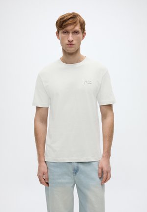 Biała bawełniana koszulka z okrągłym dekoltem i krótkimi rękawami, z małym czarnym nadrukiem tekstowym na lewej stronie klatki piersiowej.