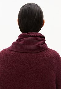 Bordeauxkleurige sjaal met een gestructureerd, gebreid ontwerp is om de nek gewikkeld, gecombineerd met een fuzzy bordeauxkleurige trui. Achteraanzicht.