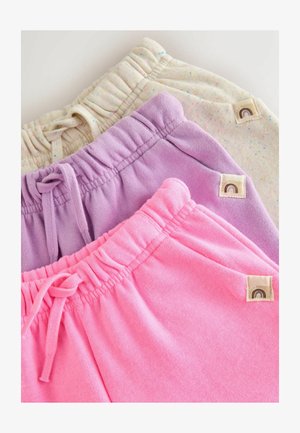 Trīs salocītu sporta bikses: vienas bēšā ar punktiem, vienas lavandas krāsā un vienas spilgti rozā, ar elastīgām jostām un auklītēm uz balta fona.