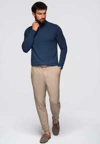 Laivastonsininen poolopaita, slim-fit vaaleanbeige housut ja harmaat mokkakengät. Yksinkertainen muotoilu, sileä pinta, ei kuvioita tai koristeita.