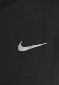 Srebrne logo swoosh Nike, umieszczone na czarnej tkaninie, podkreślające tożsamość marki w odzieży sportowej.