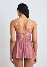 Babydoll rosa transparente con detalles de encaje y tirantes ajustables. La tela fluida permite un diseño ligero, con un corte bajo en la espalda.