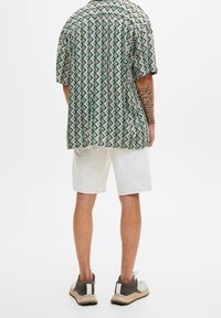 Chemise à manches courtes avec un motif géométrique en vert, noir et crème, assortie à un short blanc et des baskets aux tons multiples.