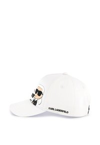 Witte baseballpet met een cartoonontwerp van een figuur in donkere zonnebrillen. Tekst "KARL LAGERFELD" in het zwart langs de zijkant.