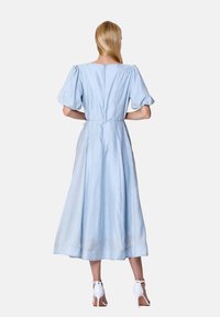 Robe longue bleu clair avec une taille cintrée, des manches bouffantes et une fermeture éclair au dos. Tissu doux et lisse avec une silhouette fluide. Présente un ourlet au niveau des chevilles.