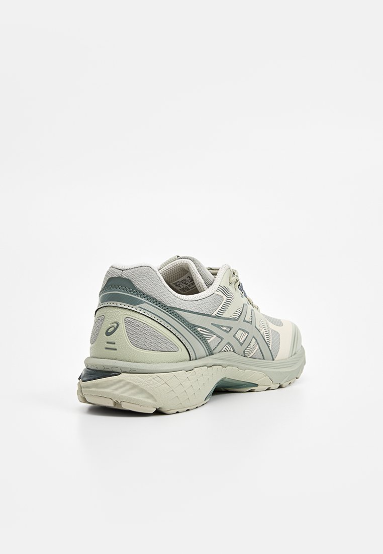 Baskets de sport gris clair avec accents turquoise, panneaux en maille, semelle rembourrée et design à lacets, présentées depuis un angle arrière sur fond blanc.