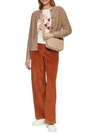 Beiger Cardigan aus strukturiertem Material, weißes Graphic-T-Shirt, orangefarbene Cordhosen, beige Umhängetasche und weiße Sneaker.