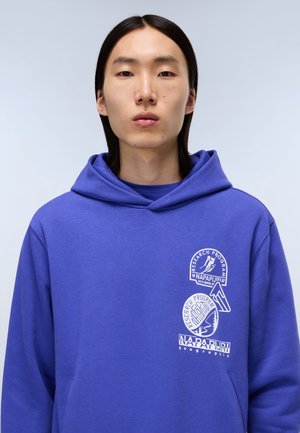 Purple hoodie featuring a kangaroo pocket, drawstring hood, and white logo prints on the chest. Smooth fabric texture.