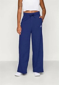 Temno modri široki trenirki z belimi stranskimi črtami in elastičnim pasom z vrvico. Minimalistični logo blizu bokov.