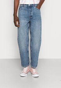 Ljust blå denimjeans med rak benform, med fem fickor och knappert stängning. Bärs med rosa högklackade sneakers.
