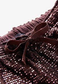 Gros plan sur un tissu à sequins violet foncé avec une taille froncée et un ruban assorti noué en nœud.