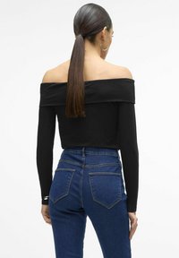 Mustat olkaimeton pitkähihaiset paita yhdistettynä korkeavyötäröisiin sinisiin farkkuihin, joissa on napakka muotoilu ja minimaalinen ommelkoristelu.