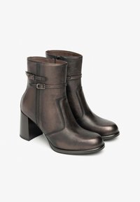 Bottines en cuir marron avec une finition lisse, dotées de doubles sangles à boucle et d'un talon carré. Détail de zip sur le côté pour un enfilage facile.