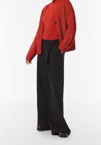 Chaqueta de punto roja con cuello redondo, cierre de botones, combinada con un jersey de cuello alto rojo ajustado y pantalones negros de pierna ancha y cintura alta.