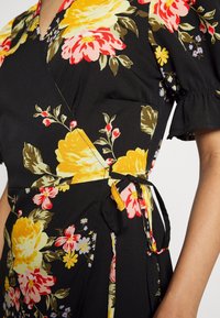 Svart klänning med stora gula, rosa och röda blommönster, korta volangärmar och en knytband detaljerad på sidan vid midjan.