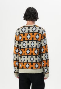 Strikket genser med strukturert mønster i oransje, svart, hvitt og beige, med rund hals og ribbestrikkede ermer og kant.