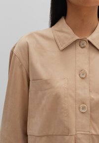 Beige overhem met een kraag, een borstzak en een soepele textuur. Heeft lichte knopen en eenvoudige stiksels.