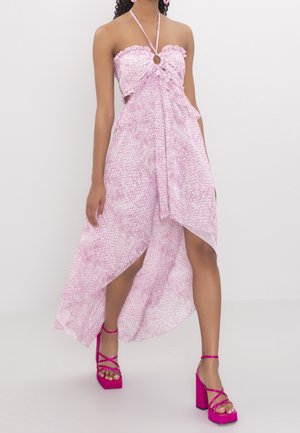 Woman wearing pink halter-neck dress with ruffles and high-low hem, paired with bright pink platform heels, standing against plain background.