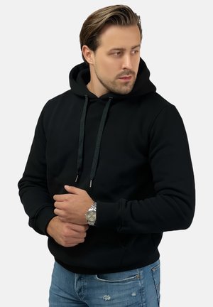 Black hoodie with a drawstring hood, ribbed cuffs, and a front pocket. Worn with light blue distressed jeans and a silver watch.