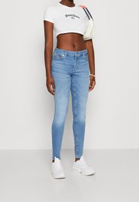 Jeans ajustados de color azul claro con cintura media, que presentan los lazos para cinturón y un diseño de cinco bolsillos. Combinados con una camiseta corta blanca y zapatillas blancas.