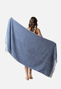 Manta de rayas azules y blancas sostenida, con un tejido texturizado y bordes con flecos, que presenta un caído suave y un diseño ligero.